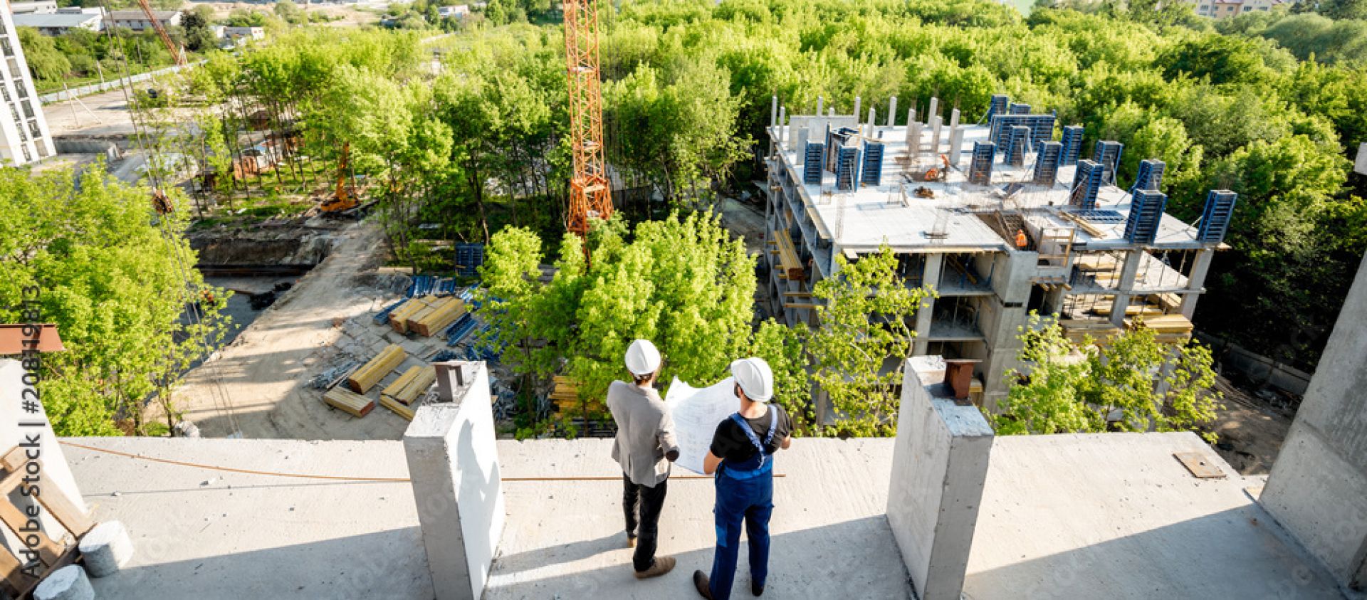 Top view on the construction site of residential buildings on the green area with two workers looking on the construction process