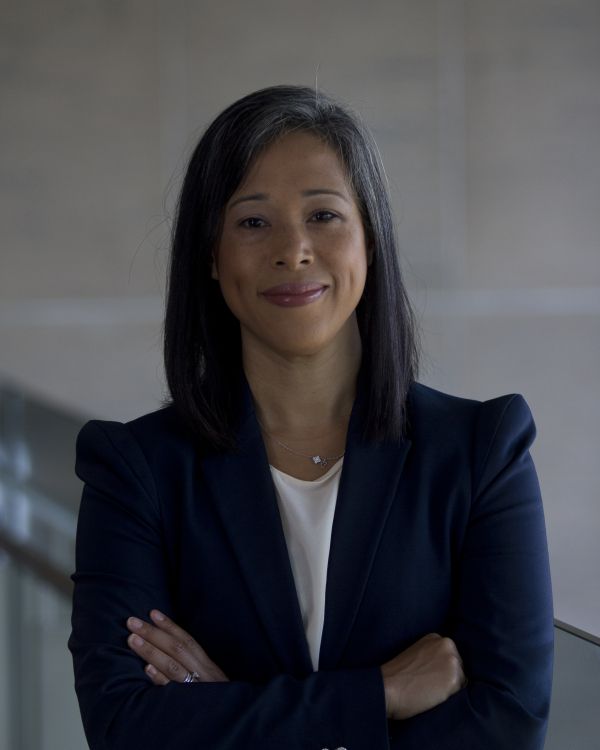 Pia Chin headshot. Pia is standing with her arms crossed, smiling at the camera. She is wearing a dark blue blazer with a white shirt.