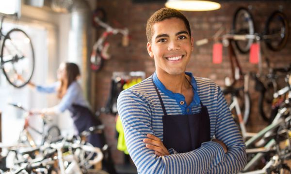 Black man crosses his arm smiling in front of bike shop